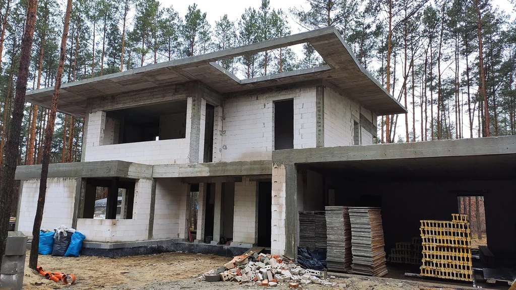 Stan surowy z garażem i otworem w dachu; w garażu składowane panele szalunkowe