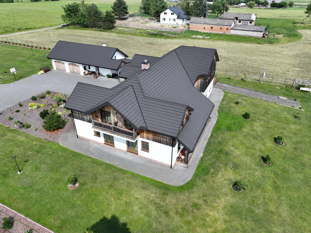 Ujęcie z drona z góry: dach domu i układ bryły budynku, obok budynek garażowy i drogi dojazdowe