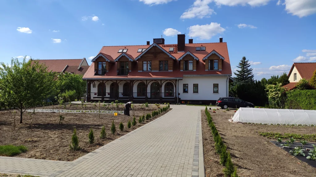 Tylna elewacja domu zakonnego w Ostródzie z drewnianymi detalami i przygotowanym terenem ogrodu
