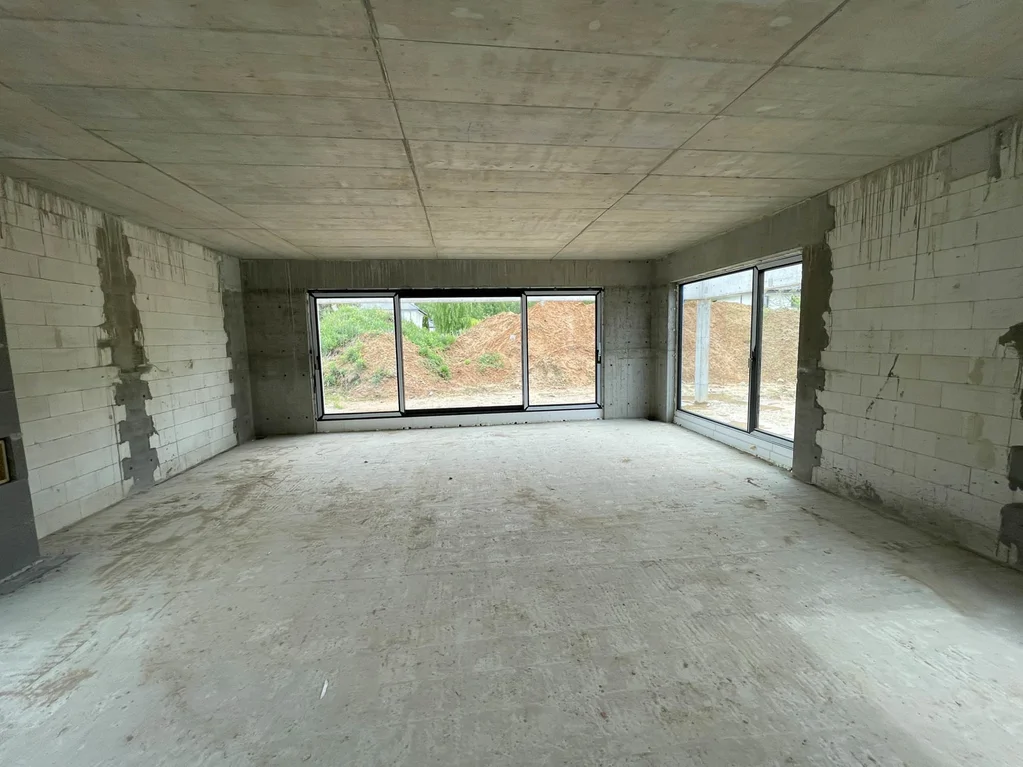 Przestronne wnętrze domu w stanie surowym z dużymi przeszkleniami i przygotowaniem do dalszych prac wykończeniowych