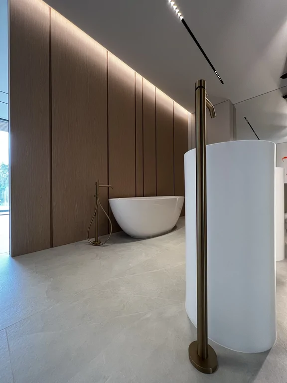 Zbliżenie na wysoką baterię i umywalkę cylindryczną. Spójny minimalizm i wykończenia w tonacji szczotkowanego złota/mosiądzu.