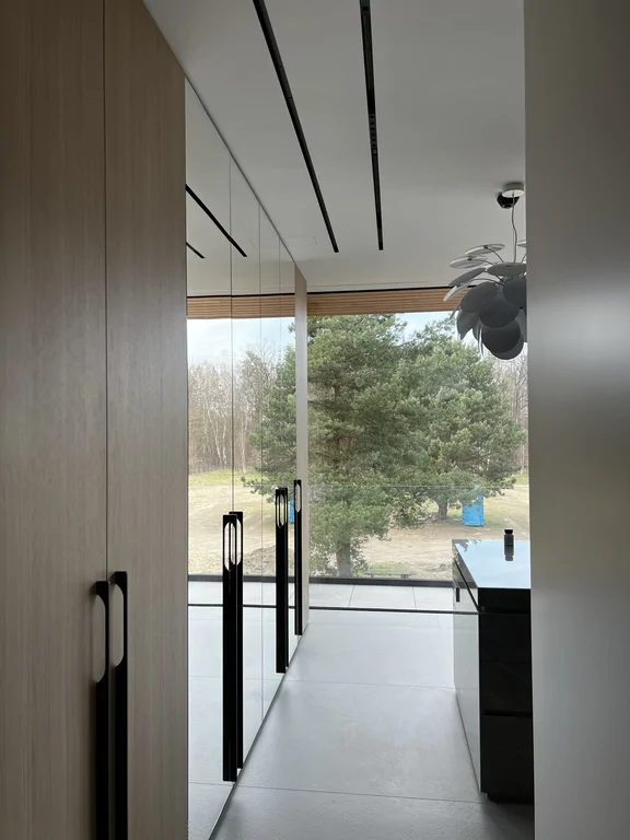 Widok w kierunku strefy kuchennej, z akcentem na czarne uchwyty, szkło i posadzkę wielkoformatową.