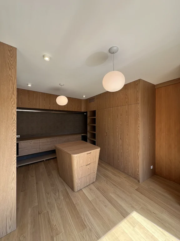 Nowoczesna garderoba z drewnianymi szafami, wyspą i oświetleniem wiszącym
