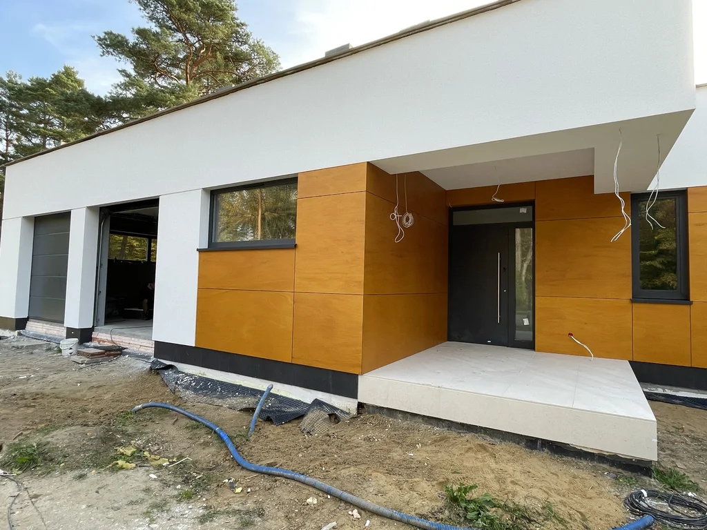 Front nowoczesnego domu z wejściem, garażem i elewacją łączącą biały tynk oraz okładzinę w kolorze drewna