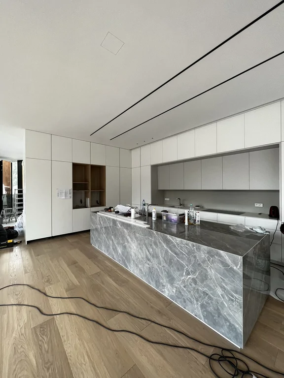 Nowoczesna kuchnia: biała zabudowa i kamienna wyspa, minimalistyczne detale w suficie.