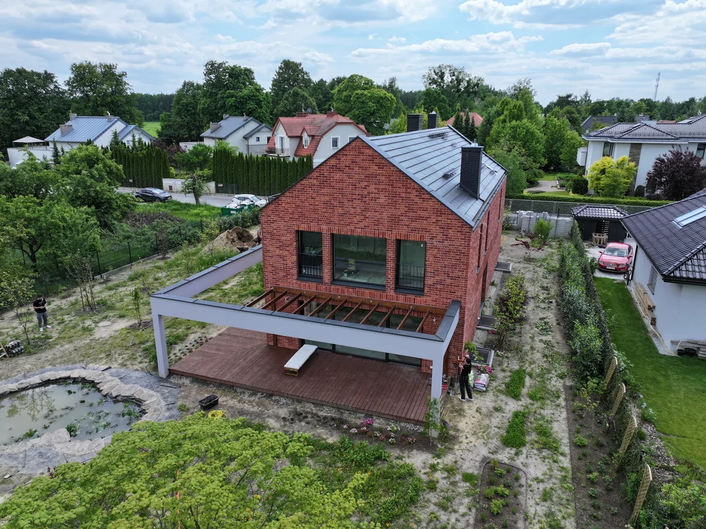 Widok z drona na tylną elewację domu z dużymi przeszkleniami, drewnianym tarasem i pergolą