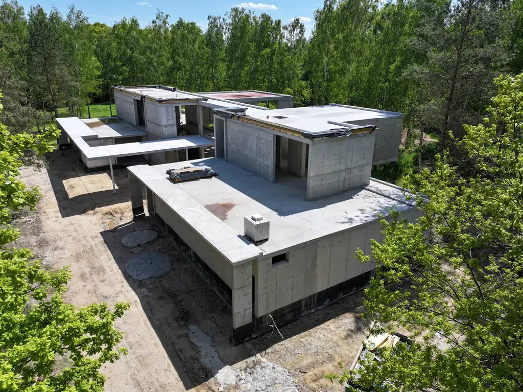 Widok z drona na nowoczesny dom żelbetowy w trakcie budowy, położony w leśnym otoczeniu.