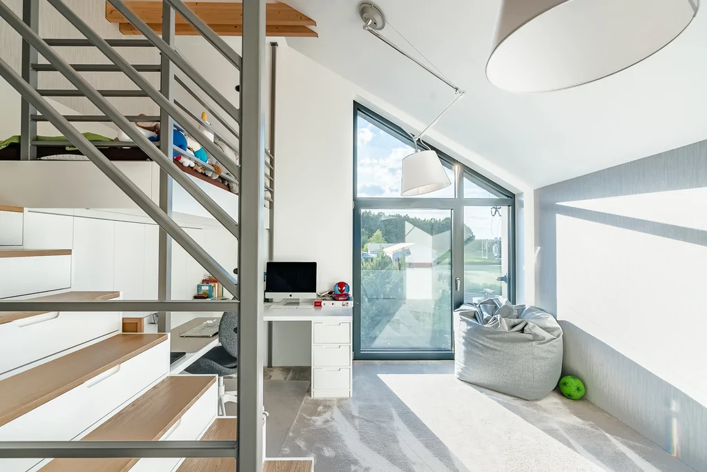 Pokój dziecięcy z antresolą, schodami z szufladami, biurkiem i dużym oknem w ścianie szczytowej.