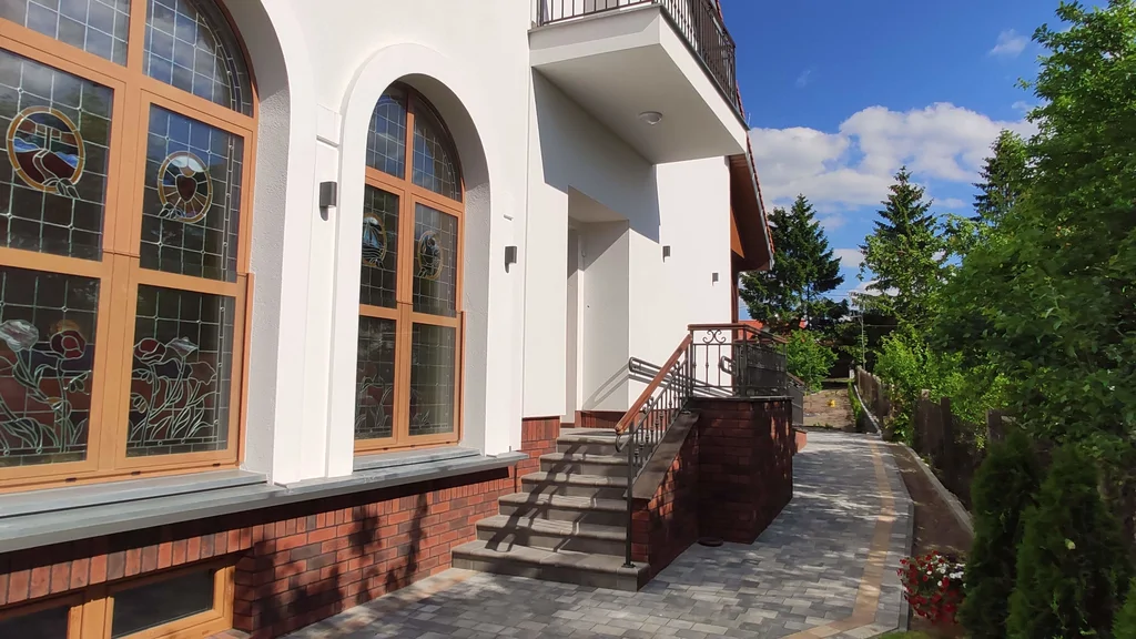 Szeroki widok na tył domu zakonnego w Ostródzie, z alejką z kostki i ogrodem przed budynkiem