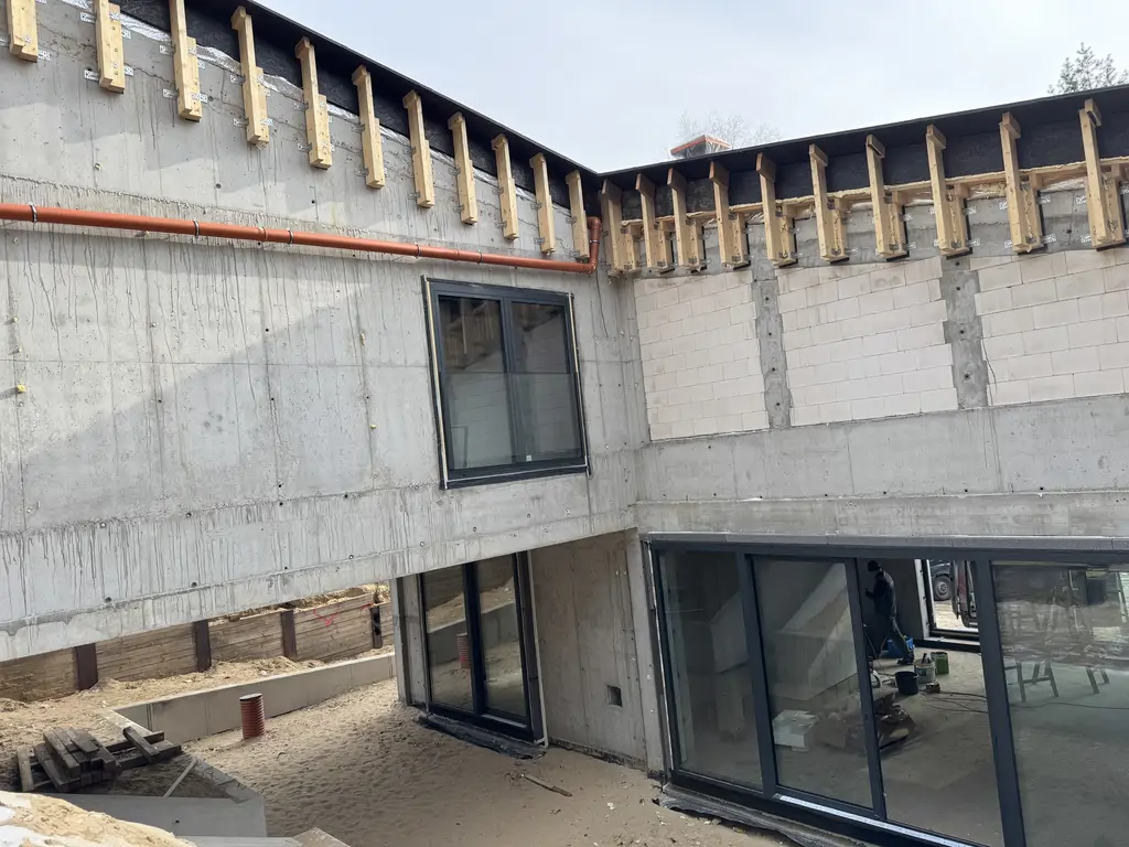 Wewnętrzne patio z zamontowaną stolarką aluminiową, żelbetowymi ścianami i rurą spustową.