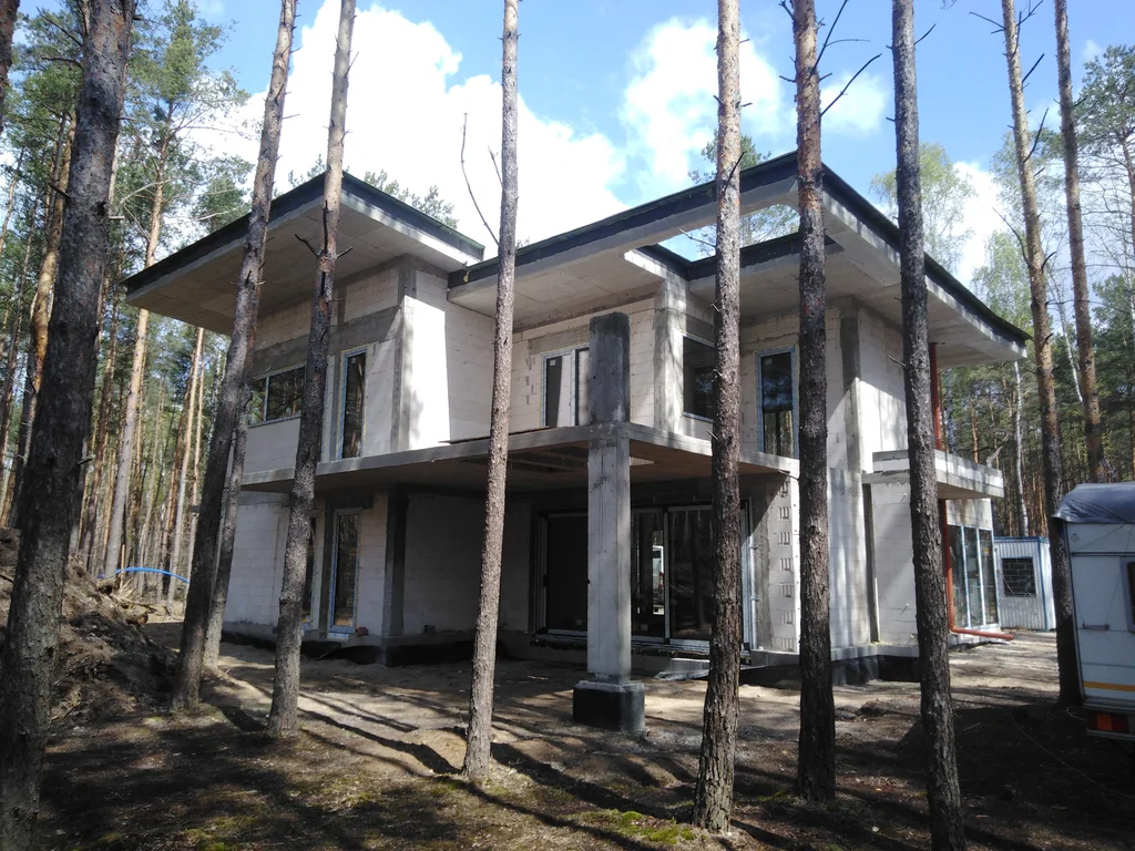 Dom podczas montażu stolarki okiennej; płaskie dachy i nadwieszenia w leśnym otoczeniu