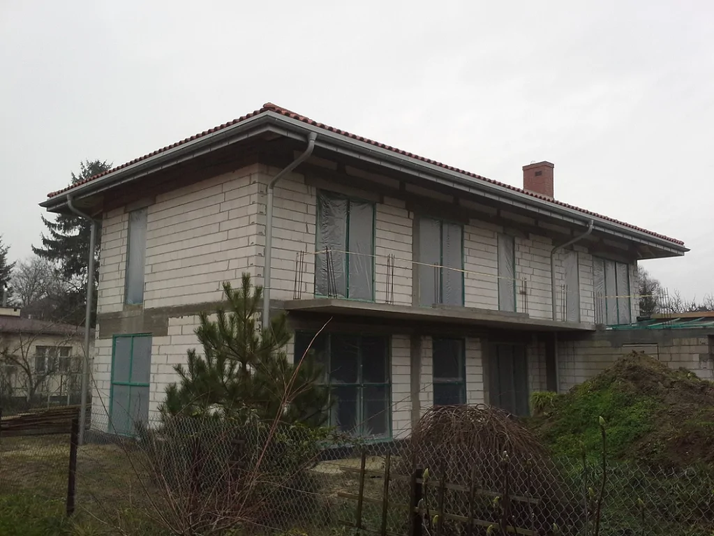 Budowa Domu jednorodzinnego widok z zewnątrz, wykonane mury oraz elementy konstrukcyjne; gotowy dach zaślepione otwory okienne