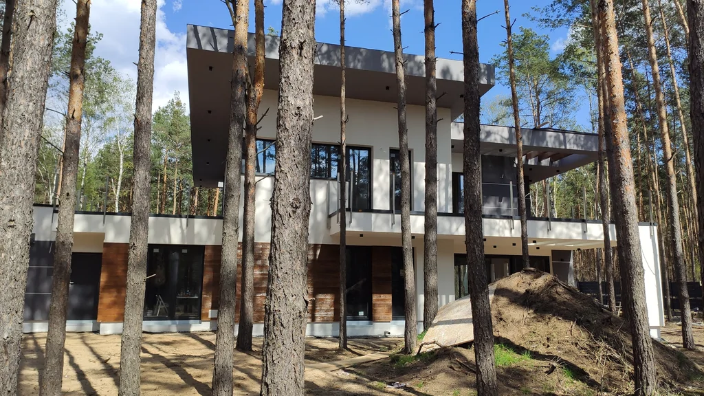 Elewacja frontowa gotowego domu z drewnianą okładziną i dużymi przeszkleniami, leśna działka