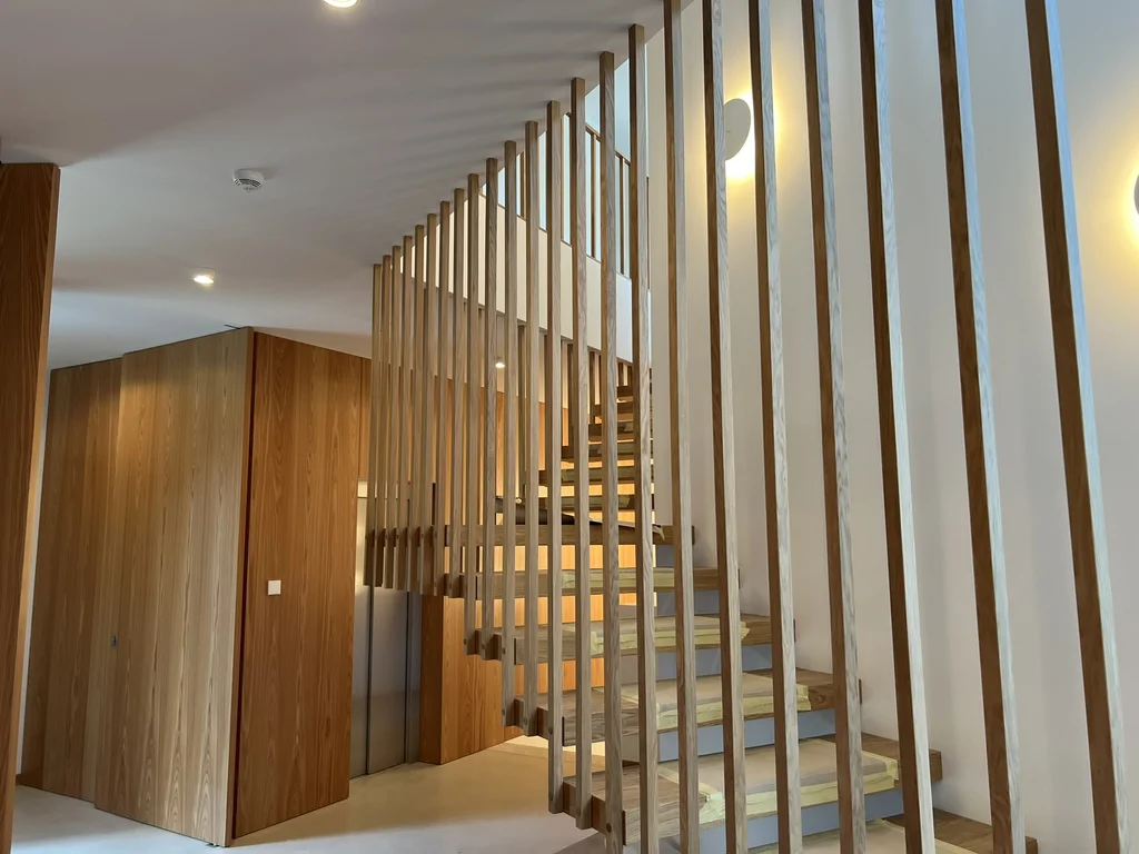 Nowoczesne schody z drewnianymi stopniami i pionowymi lamelami we wnętrzu domu