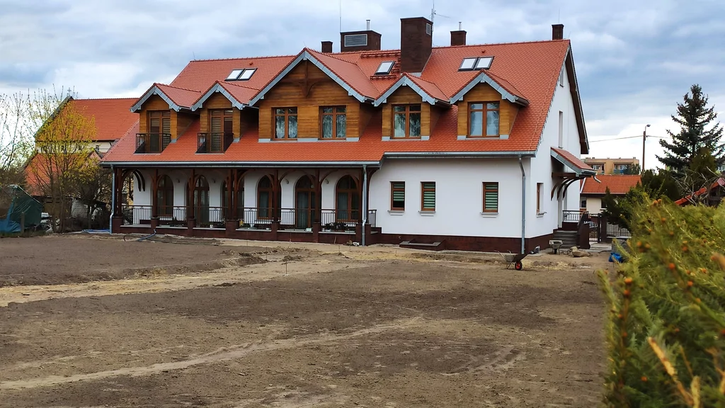 Boczna ścieżka przy domu zakonnym w Ostródzie, ze schodami i wysokimi oknami z łukami oraz witrażami