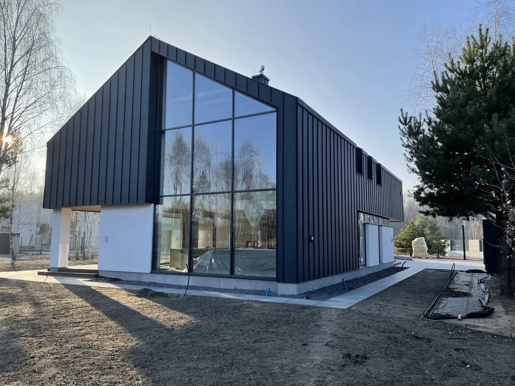 Nowoczesny dom z wysokim przeszkleniem i czarną elewacją, widok w słoneczny dzień