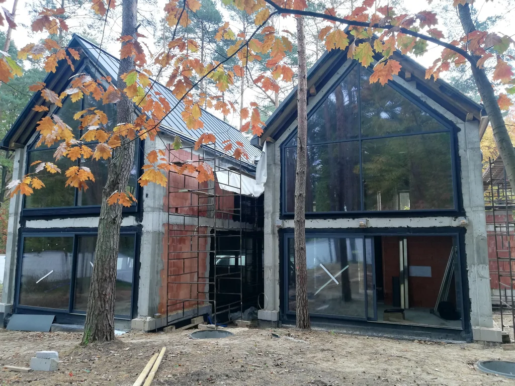 Dom jednorodzinny w Magdalence w trakcie prac elewacyjnych z dużymi przeszkleniami i dwiema bryłami pod dachem dwuspadowym