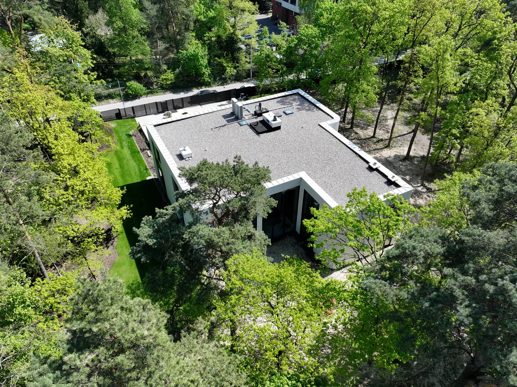 Widok z góry na tył i bok budynku z płaskim dachem, dużymi przeszkleniami i leśnym krajobrazem wokół