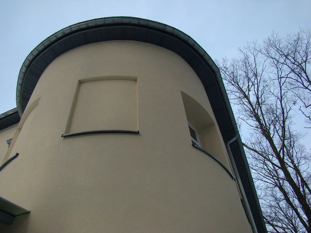 Zaokrąglony narożnik budynku i okap dachu widziane z dołu; detal elewacji po remoncie.