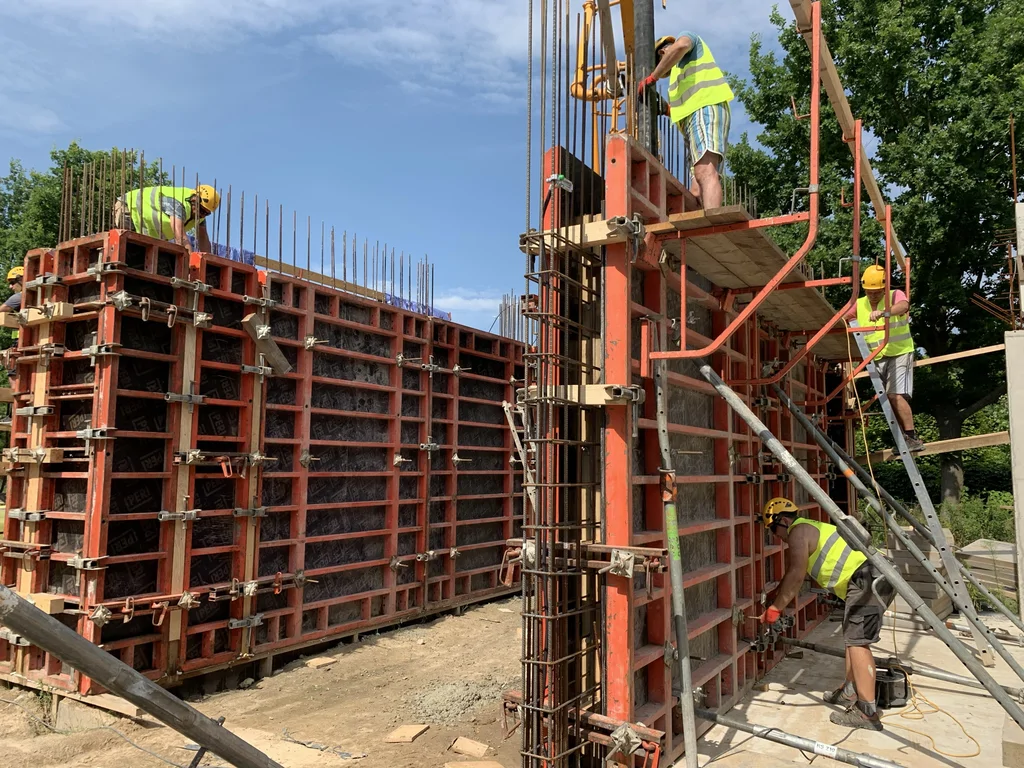 Prace ekip przy szalunkach i zbrojeniu ścian oraz słupów żelbetowych – wylewanie  betonu architektonicznego