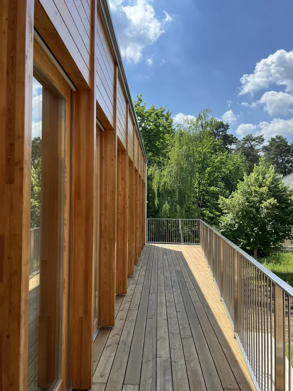 Długi balkon przy drewnianej elewacji nowoczesnego budynku z widokiem na zieleń