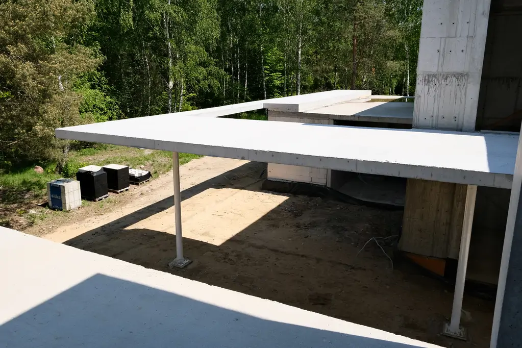 Żelbetowy podcień nowoczesnego domu w trakcie budowy z widocznym zadaszeniem i słupami konstrukcyjnymi.