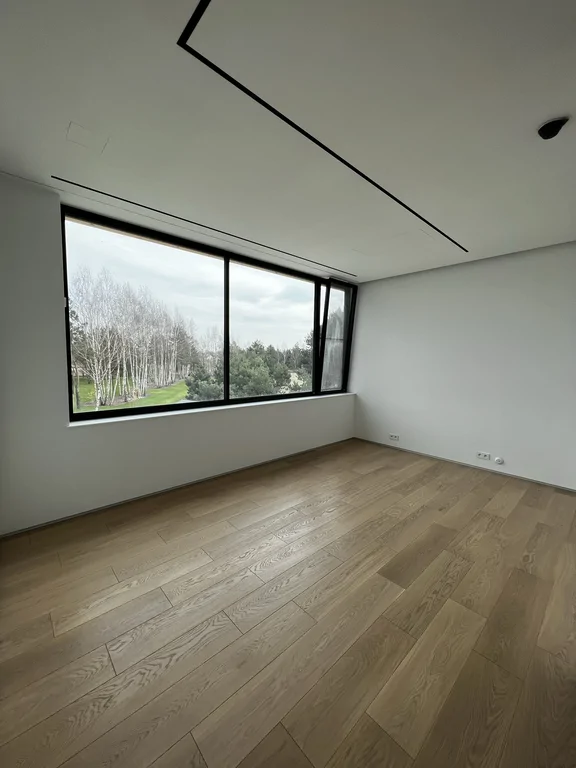 Pokój z panoramicznym oknem, dębową podłogą i liniowymi szczelinami w suficie.