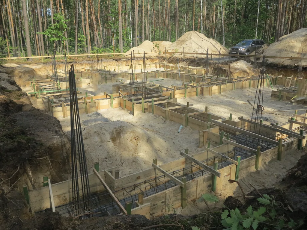 Wykopy i szalunki fundamentów zbrojonych na działce leśnej, przygotowanie do betonowania