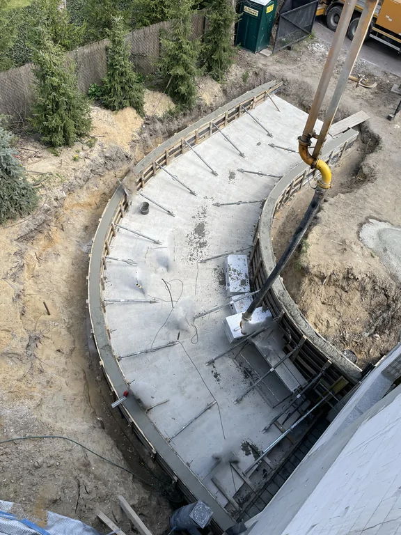 Łukowy zjazd do garażu podziemnego przy domu jednorodzinnym ze szczelną piwnicą w technologii białej wanny