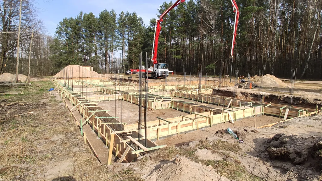 Przygotowanie do betonowania fundamentów: deskowanie, zbrojenie oraz pompa do betonu na placu budowy