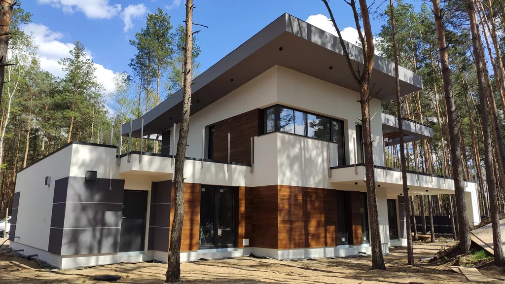 Narożnik elewacji: biała bryła, grafitowe attyki i drewniana okładzina, duże przeszklenia