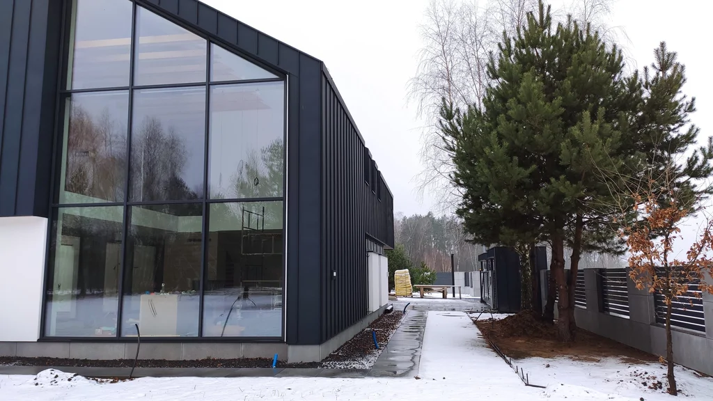 Boczne przeszklenie nowoczesnego domu i ścieżka wzdłuż elewacji, widok zimowy