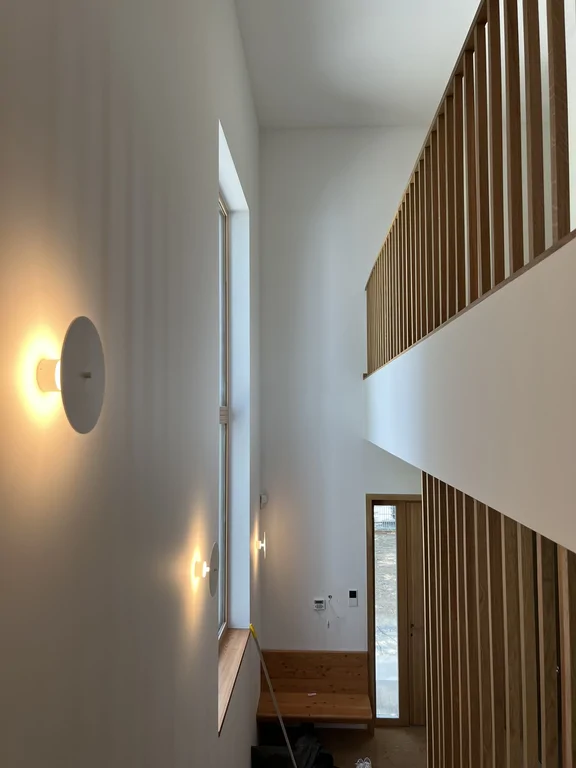 Wysoka klatka schodowa z drewnianą balustradą i nowoczesnymi kinkietami ściennymi