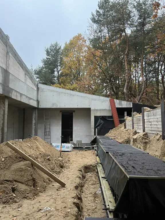 Boczny widok na zagłębioną część budynku z wykopem i przygotowaniem pod elementy żelbetowe.