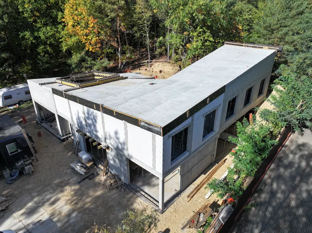 Widok na wewnętrzny dziedziniec budynku z żelbetową konstrukcją, pochyłą ścianą i otwartą przestrzenią komunikacyjną.