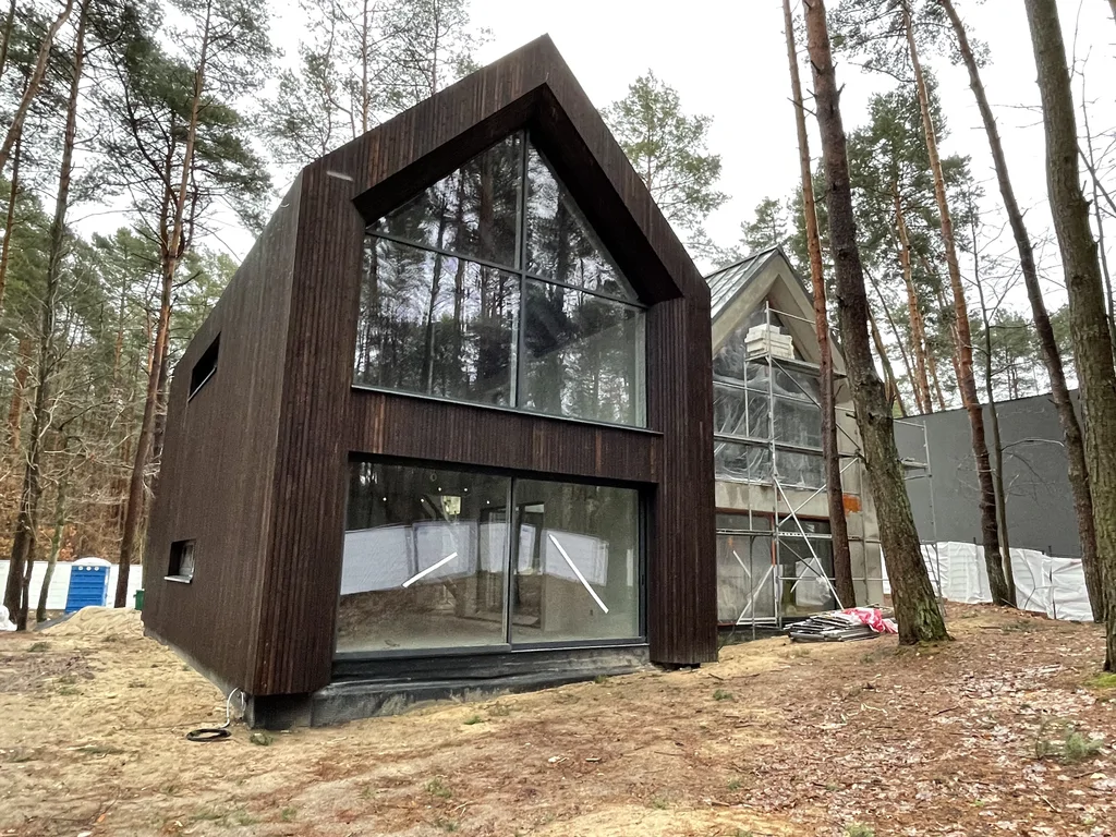 Nowoczesna drewniana bryła domu z wysokim przeszkleniem w szczycie na etapie wykończenia elewacji