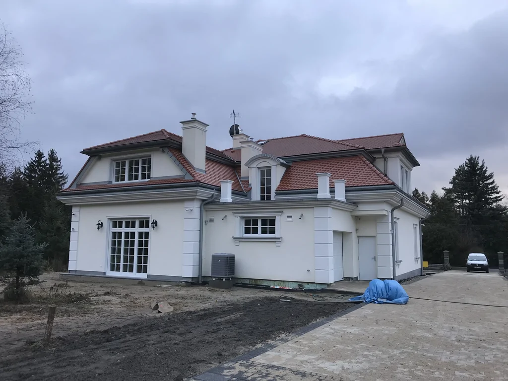 Budowa domu jednorodzinnego, styl dworkowy, dachówka z karpiówki, biała elewacja, bonie, lukarny, kominy, biała stolarka okienna 