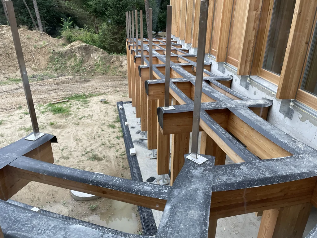 Drewniana pergola tarasowa z metalowymi słupkami i obróbkami blacharskimi w trakcie realizacji domu jednorodzinnego