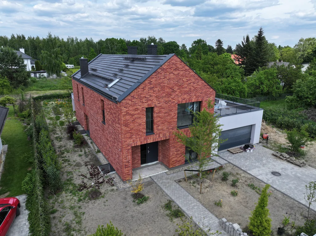 Ujęcie z drona na boczną i frontową elewację domu z ceglaną okładziną oraz podjazdem do garażu