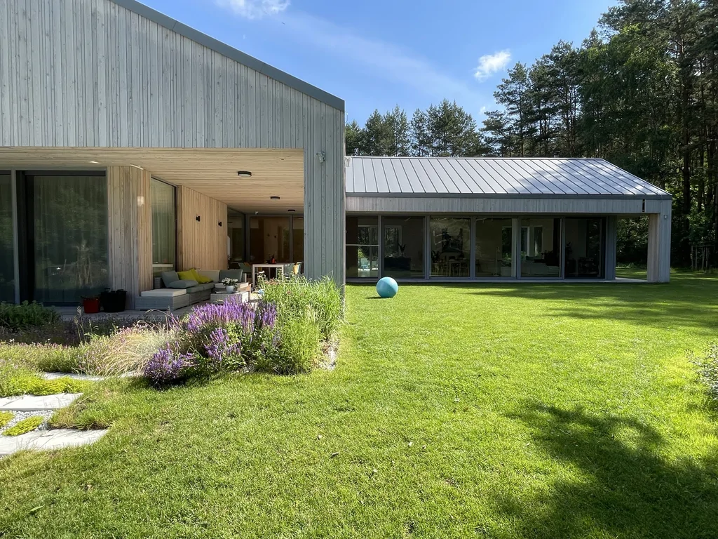 Widok ogólny budynku parterowego o rozczłonkowanej bryle – elewacja drewniana, dach na rąbek i duże przeszklenia od strony ogrodu