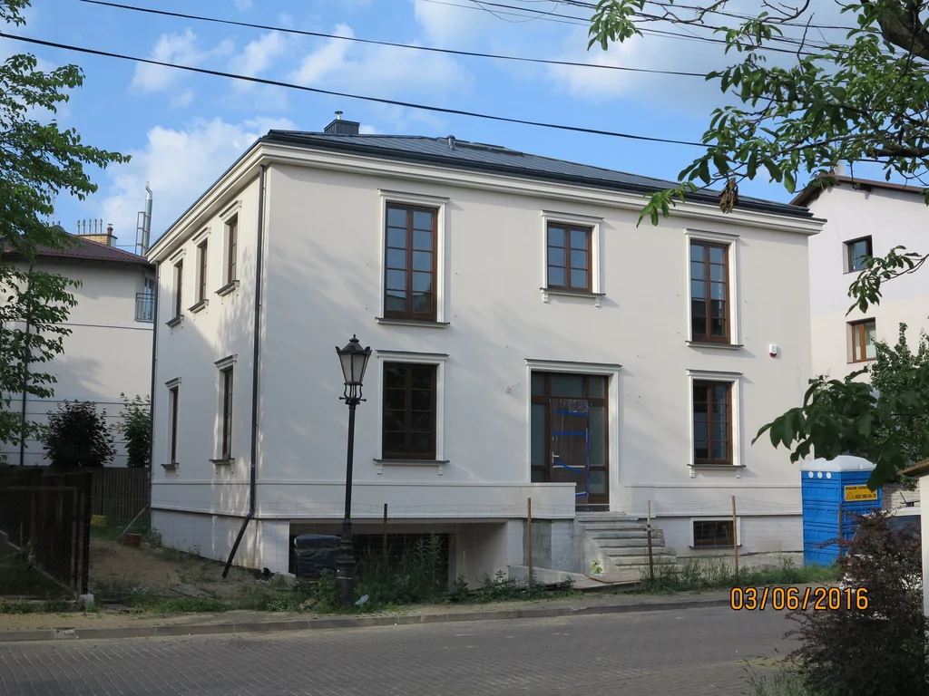 Dom jednorodzinny w stanie deweloperskim, biała elewacja, ciemna stolarka okienna, pokrycie dachowe z blachy