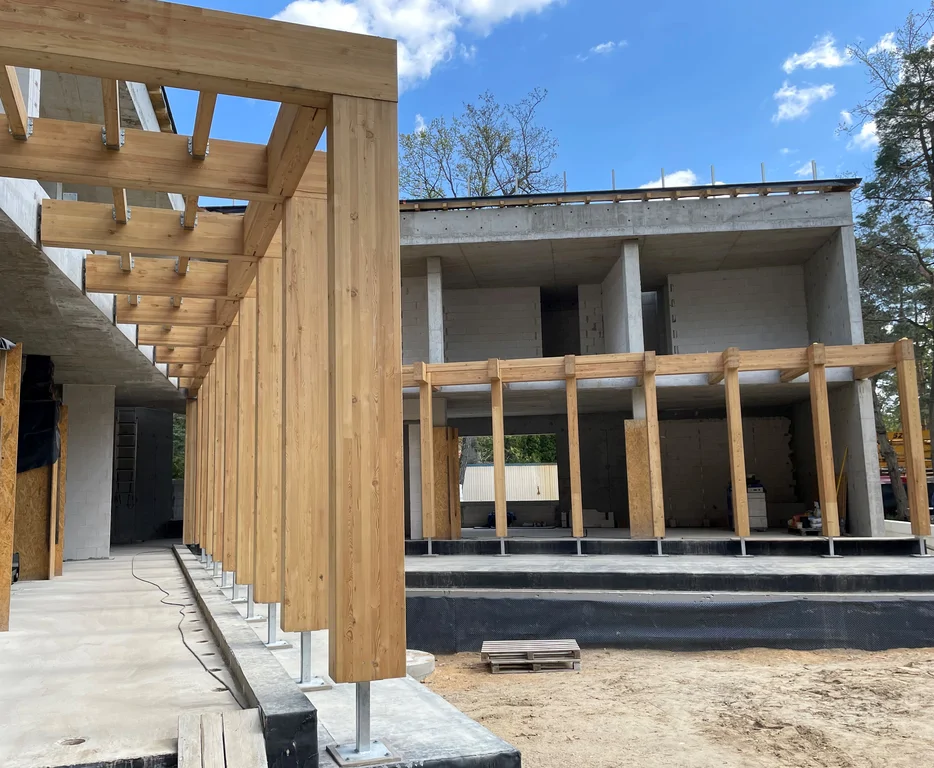 Wewnętrzny dziedziniec domu jednorodzinnego z żelbetową konstrukcją oraz drewnianymi słupami przyszłego zadaszenia tarasu