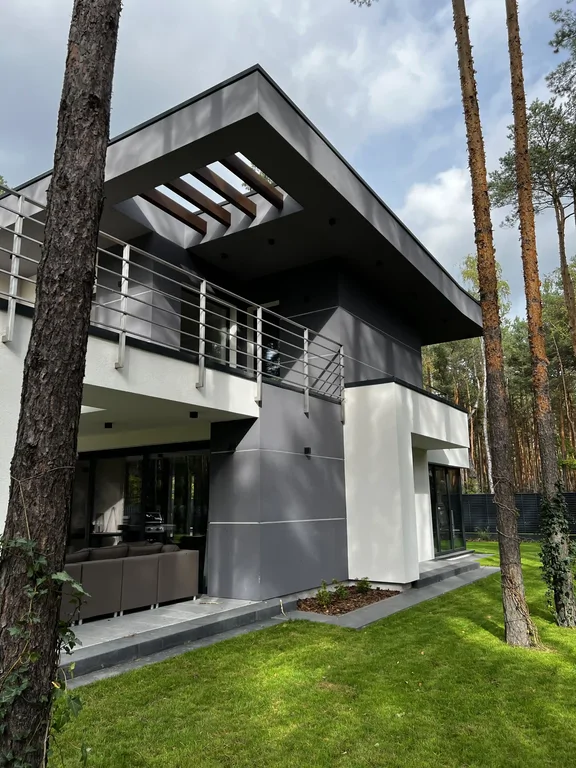 Narożnik domu z pergolą w okapie i balustradą tarasu; pod zadaszeniem strefa wypoczynku