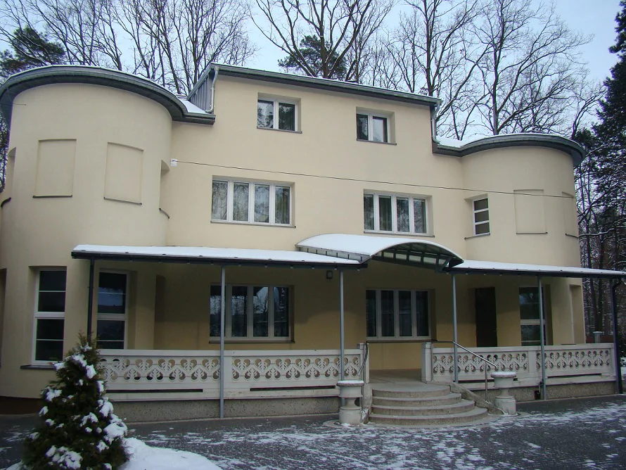 Elewacja frontowa budynku po remoncie, zimą; symetryczna bryła z zaokrąglonymi narożnikami i zadaszeniem wejścia