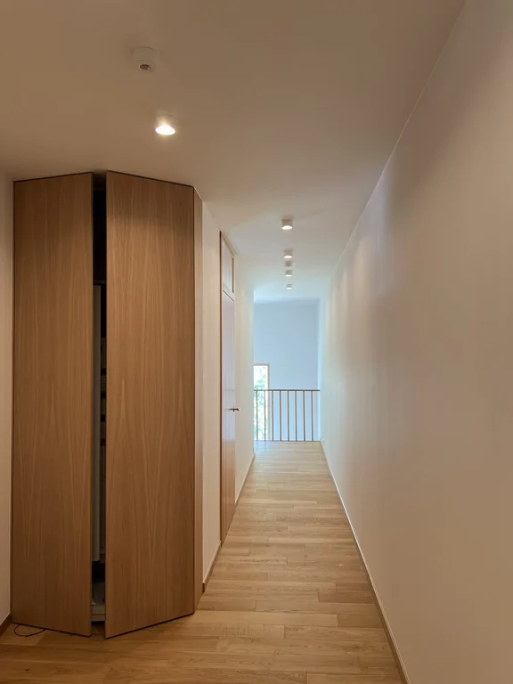 Pokój z drewnianą podłogą, białą zabudową ścienną i wejściem do łazienki