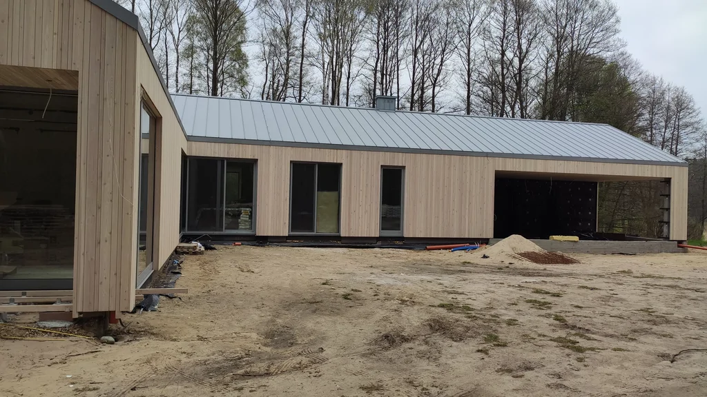 Dziedziniec domu z elewacją z pionowych desek i dużymi oknami tarasowymi