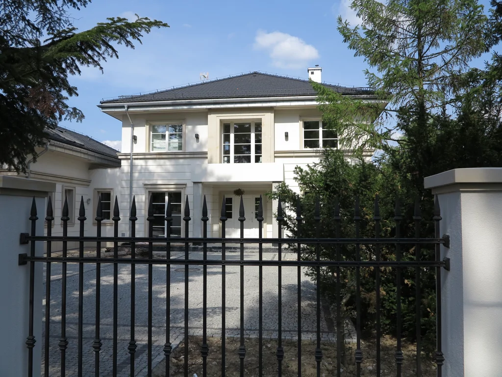 Elewacja frontowa domu jednorodzinnego, widok przez ogrodzenie na wejście główne