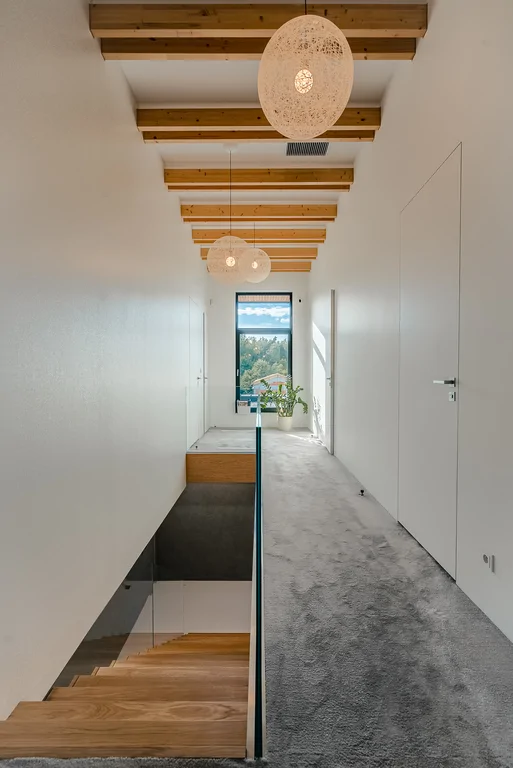 Korytarz na piętrze z wykładziną, drewnianymi belkami i zejściem schodami w dół.