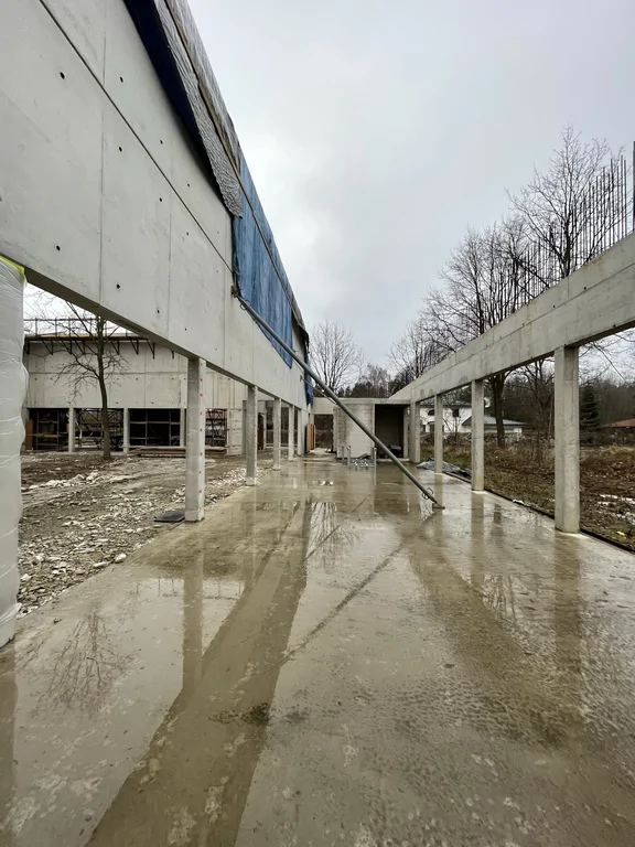 Przejście wzdłuż ściany z betonu architektonicznego na słupach żelbetowych – stan surowy, mokra płyta i stężenia montażowe