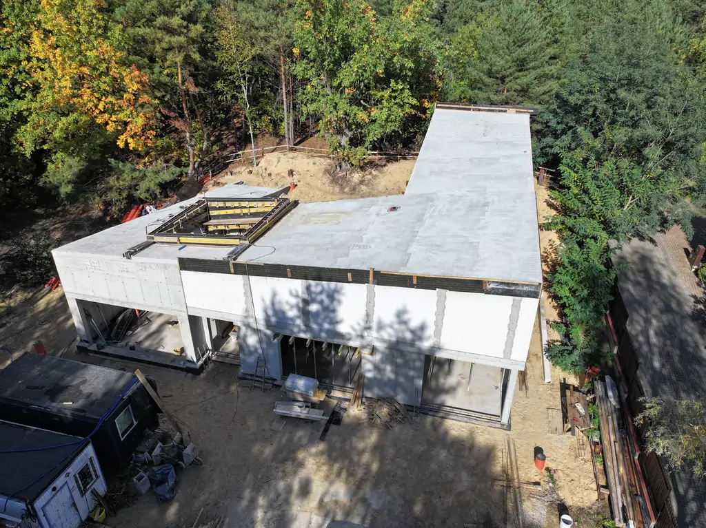 Widok z drona na elewację budynku w stanie surowym z żelbetowym szkieletem i przygotowanymi otworami pod przeszklenia.